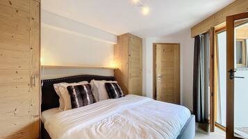 Une chambre avec un grand lit, une armoire en bois et une porte donnant sur un balcon.