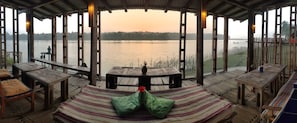 A wooden deck with a hammock and tables overlooking a lake.