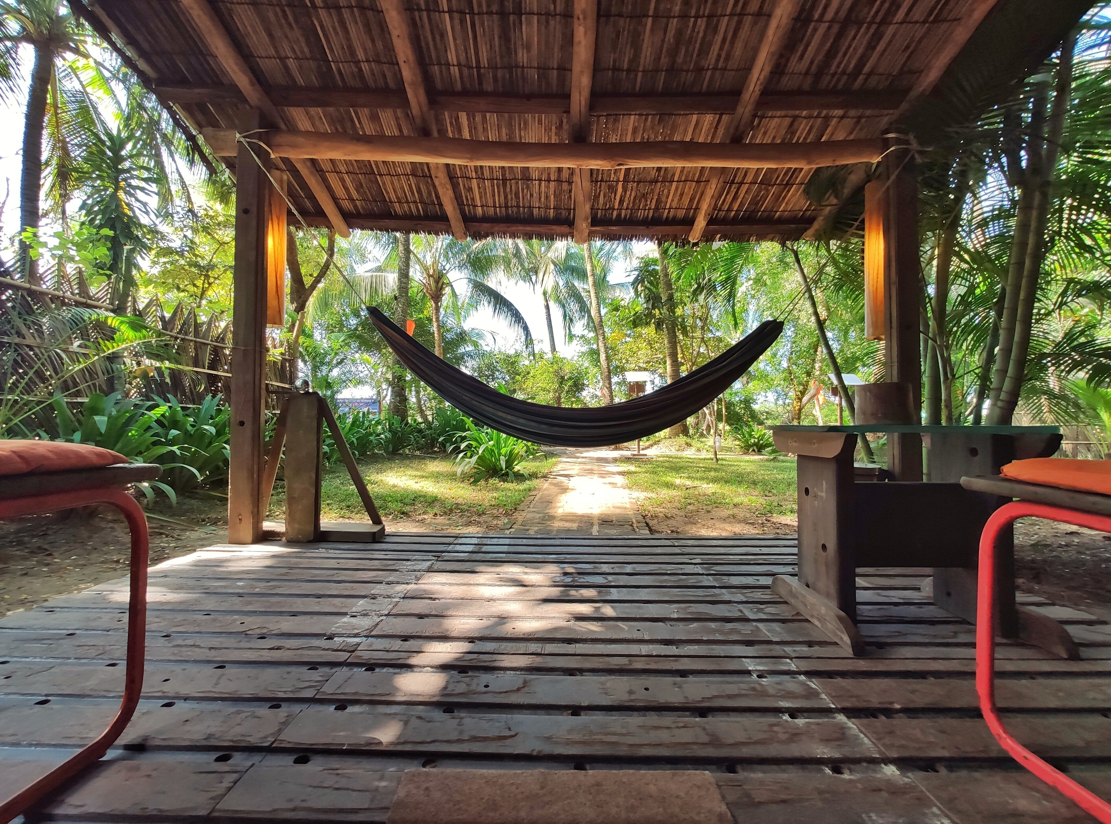 A hammock under a wooden pergola with a view of a tropical garden.