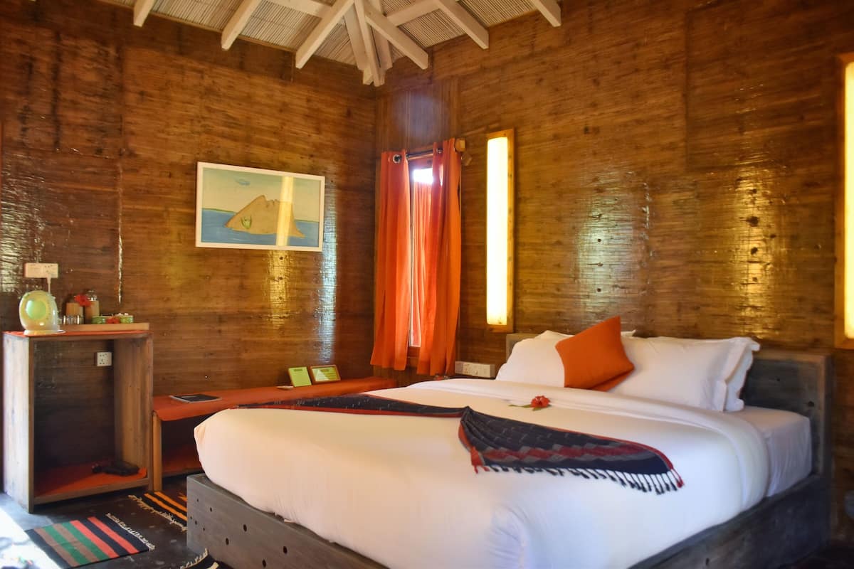 A wooden room with a bed, a small table, and a painting on the wall.