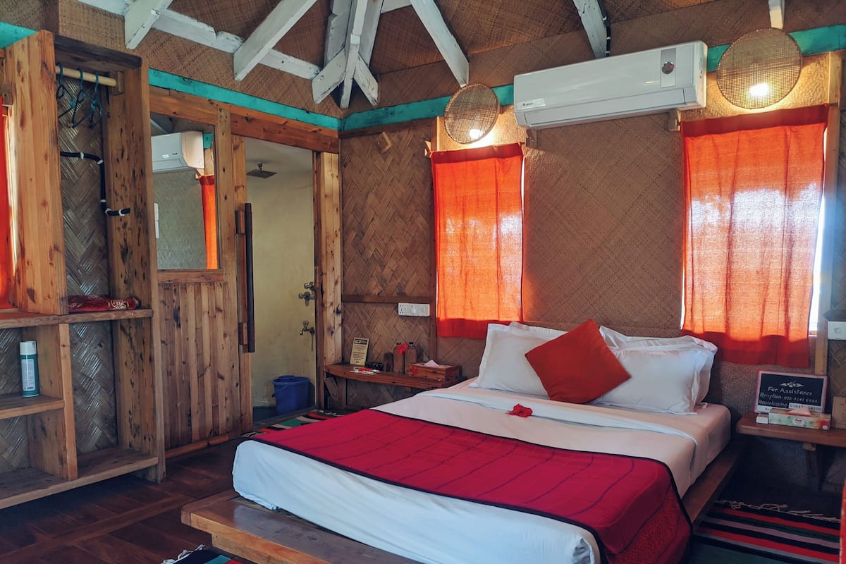 A wooden room with a bed, a nightstand, a mirror, and a window with curtains.