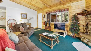 Ein gemütliches Blockhaus-Interieur mit Holzbalkendecke, Fernseher, Weihnachtstannenbaum und rustikalem Kamin.