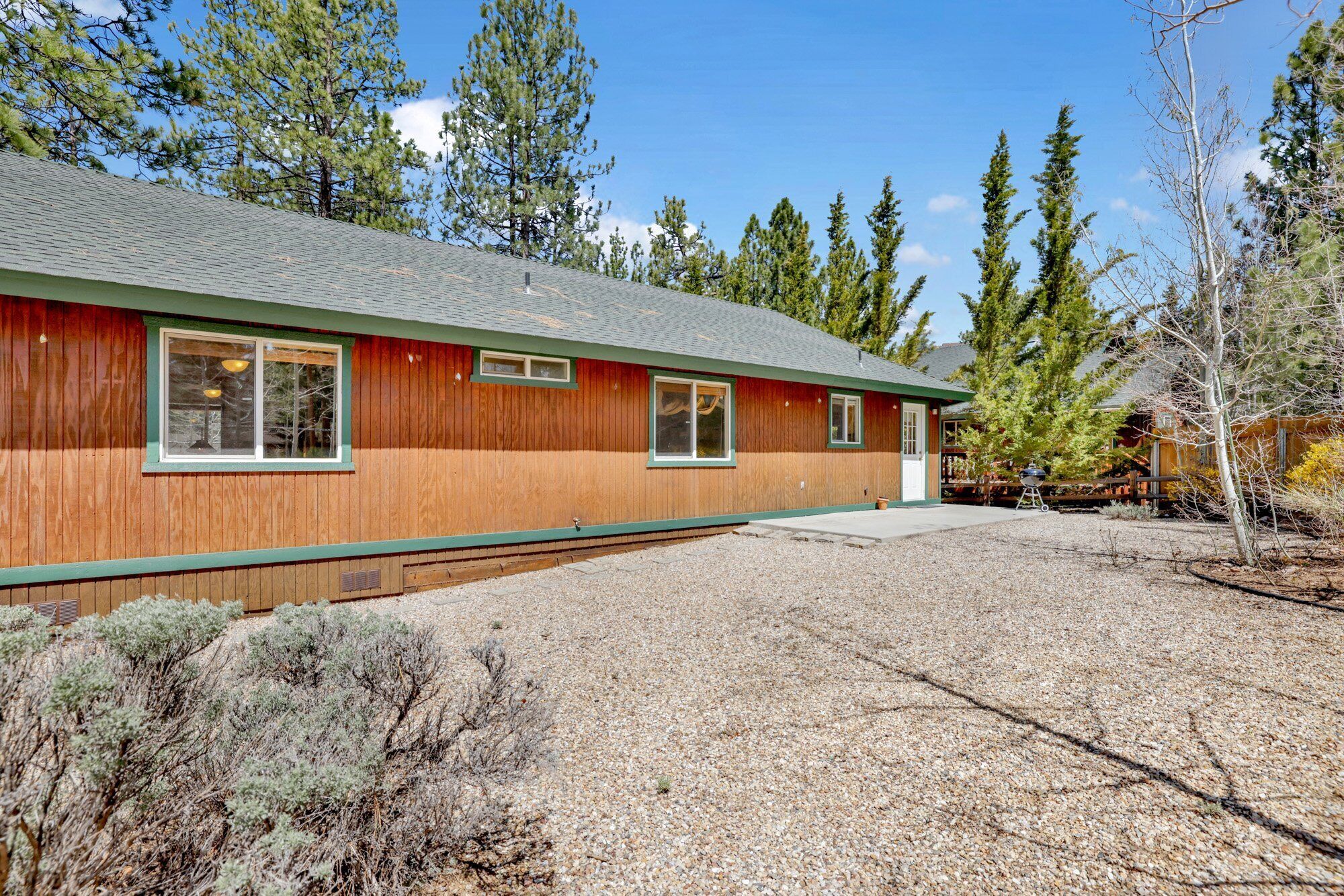 A two-story wooden house with a gravel driveway and surrounding trees.