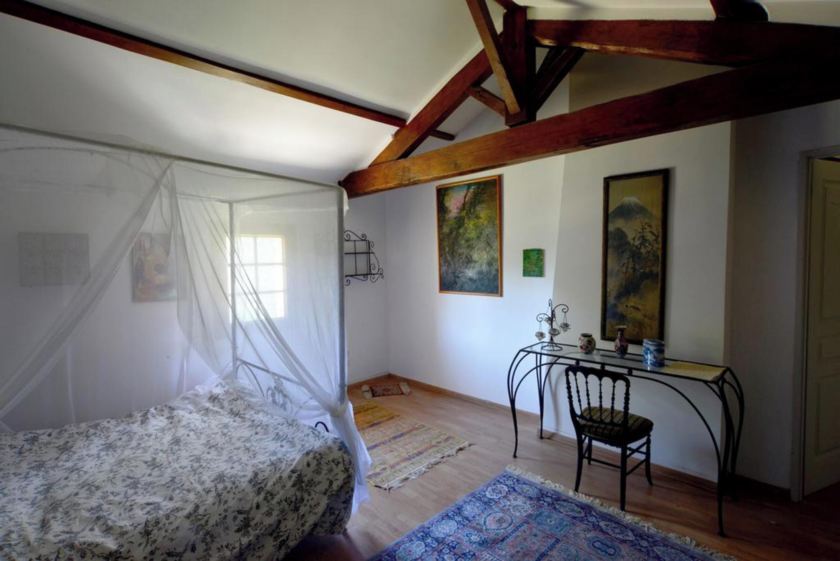 A bedroom with a canopy bed, a desk with a chair, and artwork on the walls.