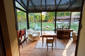 A conservatory with a view of a garden, a dining table with chairs, and a piano. - Homerez - Festive House in Callen (Callen)