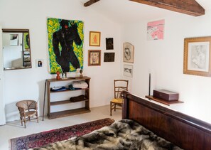 A room with a bed, a wooden headboard, a mirror, a shelf with folded clothes, a chair, and various framed artworks on the wall. - Homerez - Festive House in Callen (Callen)