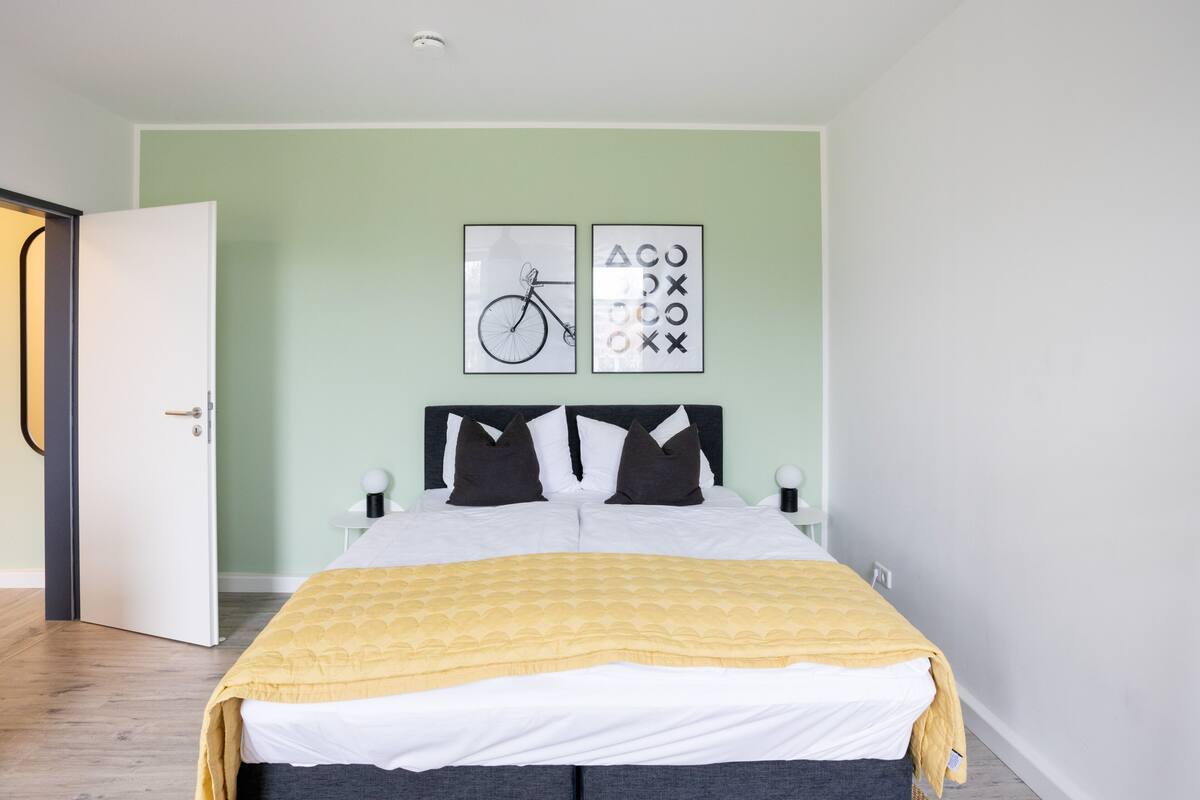 A neatly arranged bedroom with a bed, a door, and two wall-mounted artworks.