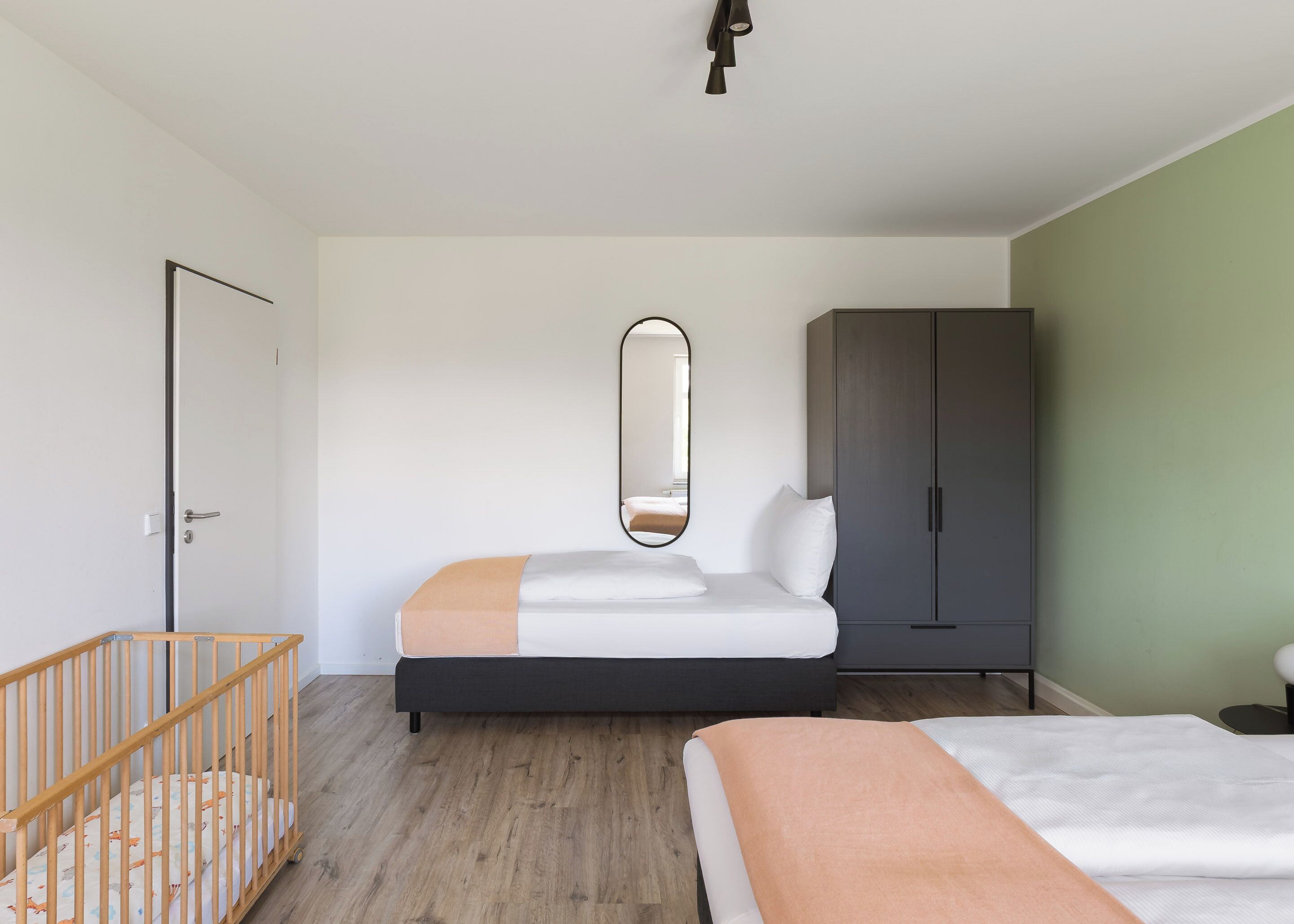 A bedroom with a bed, a crib, a wardrobe, and a mirror.