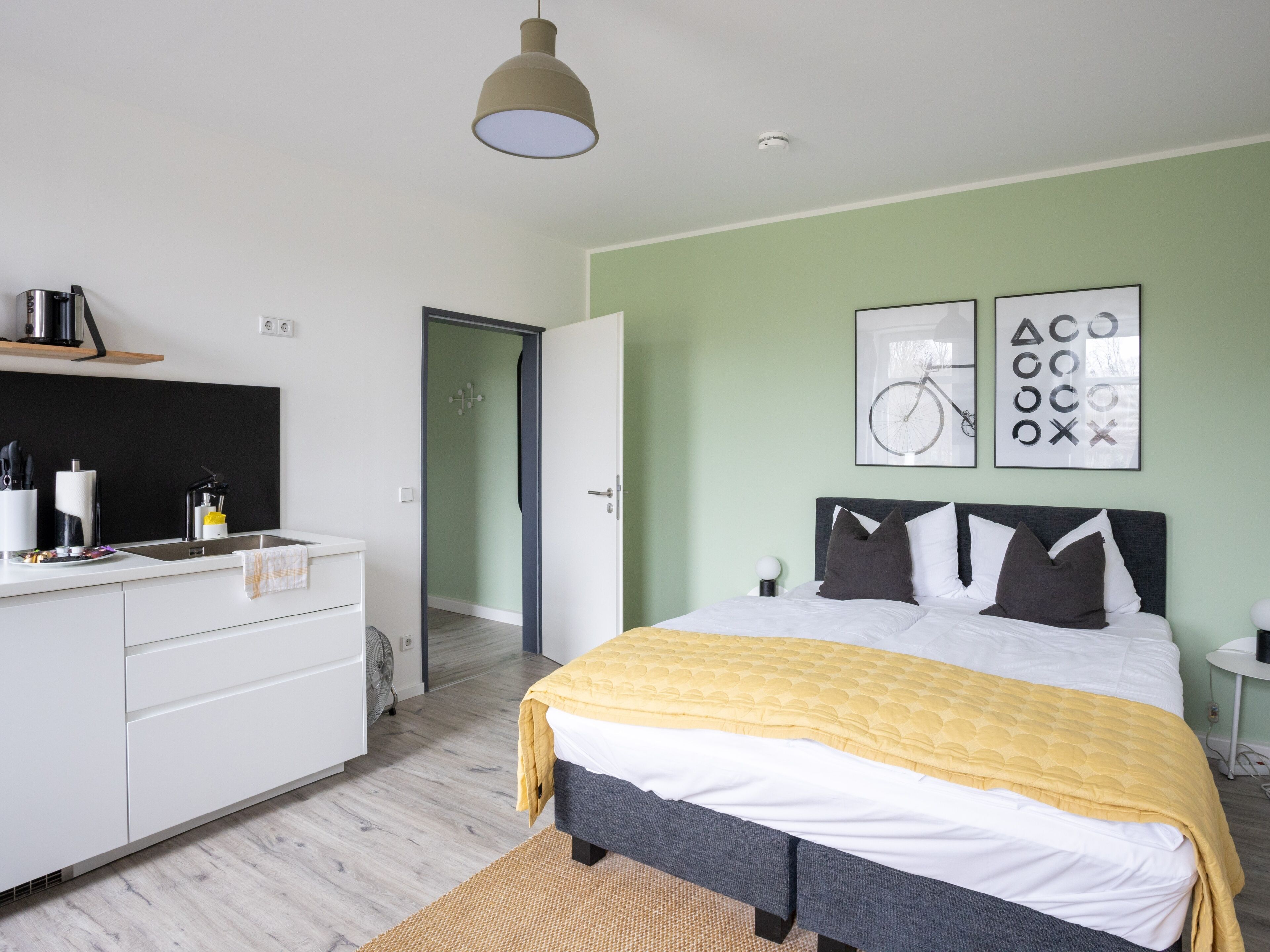 A modern bedroom with a bed, bedside tables, a wardrobe, and a door leading to another room.