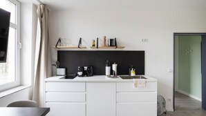 A modern kitchen with a white countertop, black backsplash, and wooden shelves above.