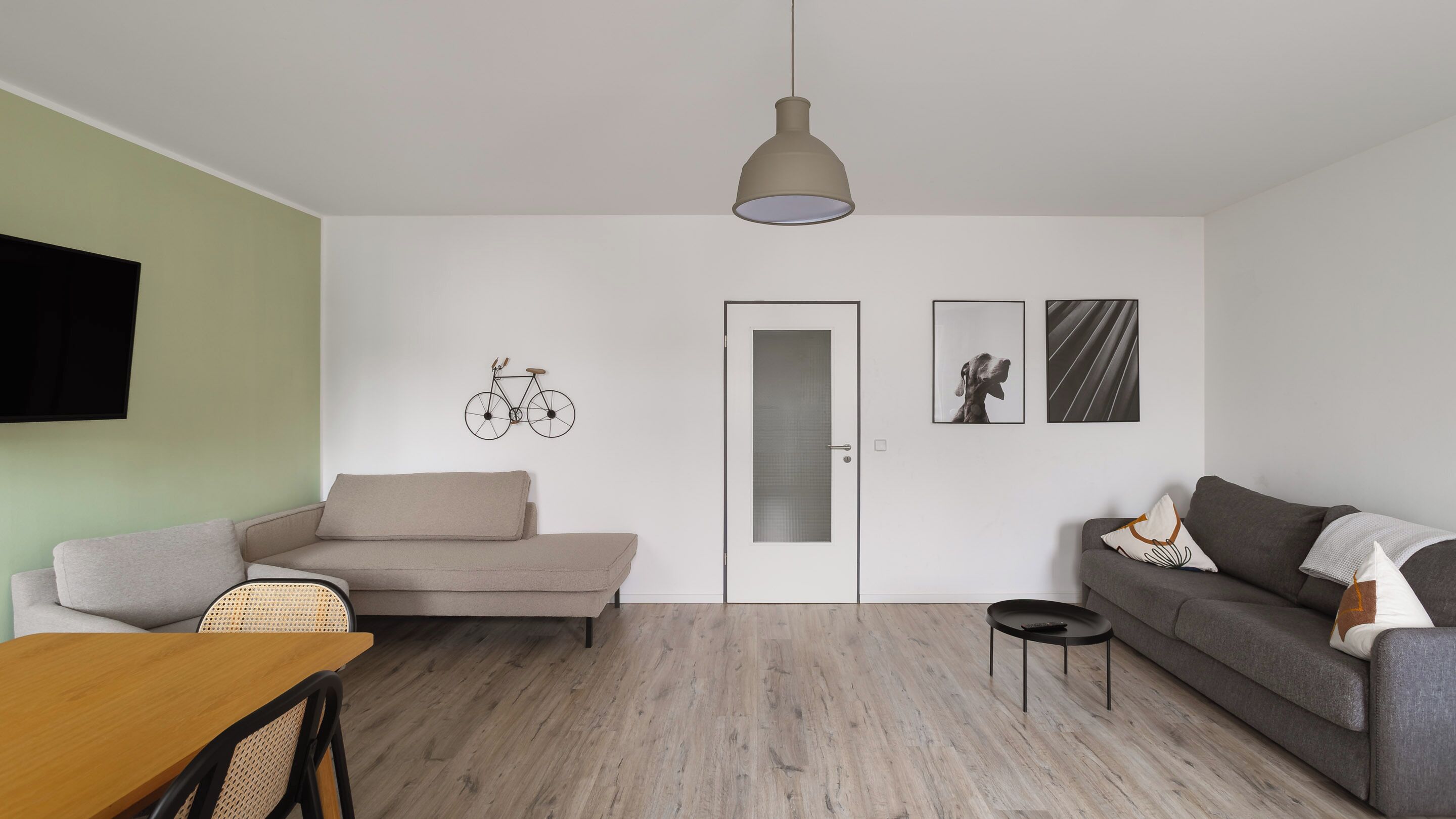 Un salon moderne comprenant un canapé, une table à manger, une table basse, un vélo fixé au mur, une porte et deux tableaux encadrés.