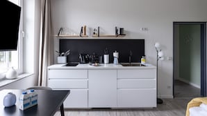A modern kitchen with a central island, white cabinetry, and a black backsplash. There are shelves above the island holding various kitchen items.