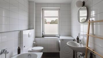 Un baño moderno con bañera, inodoro y lavamanos, que cuenta con una ventana y un espejo.
