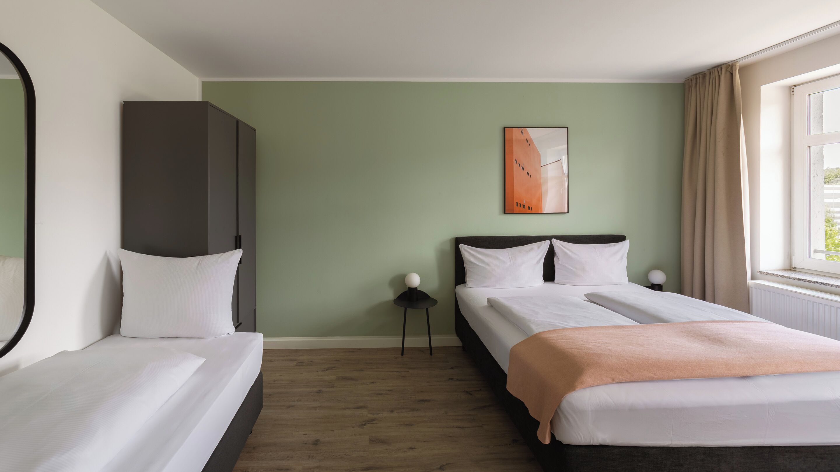 A hotel room with a bed, a bedside table, a wardrobe, and a window with curtains.