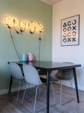 A dining area with a table and four chairs, a neon sign reading "SO SUITE", and a framed abstract artwork on the wall. - Limehome Chemnitz Hartmannstraße (Chemnitz)