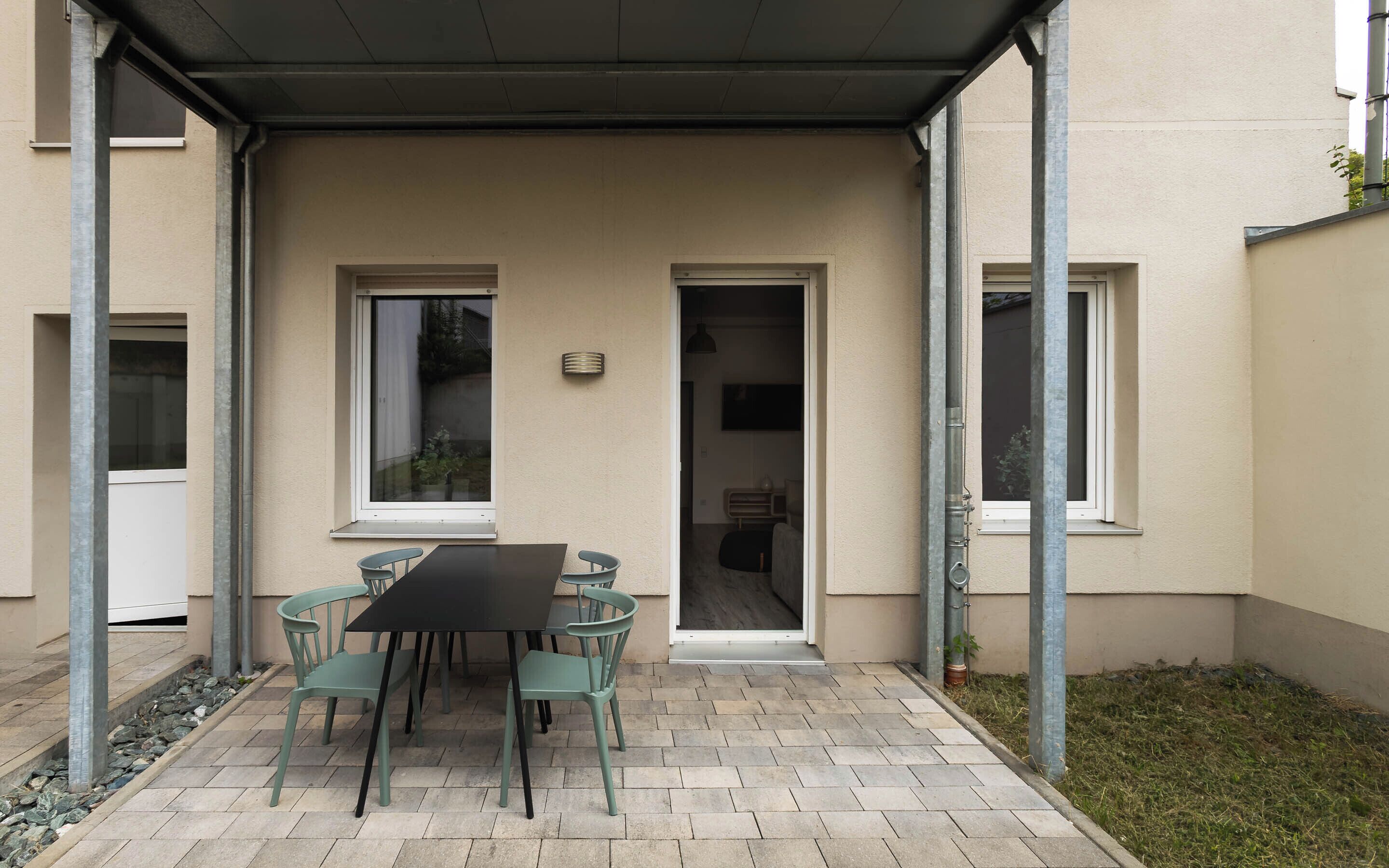 Une terrasse extérieure avec une table et des chaises, un espace abrité et l’entrée d’un bâtiment.