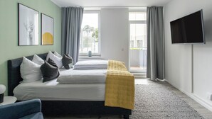 A modern hotel room with a bed, a sofa, a TV, and a view of the outside.