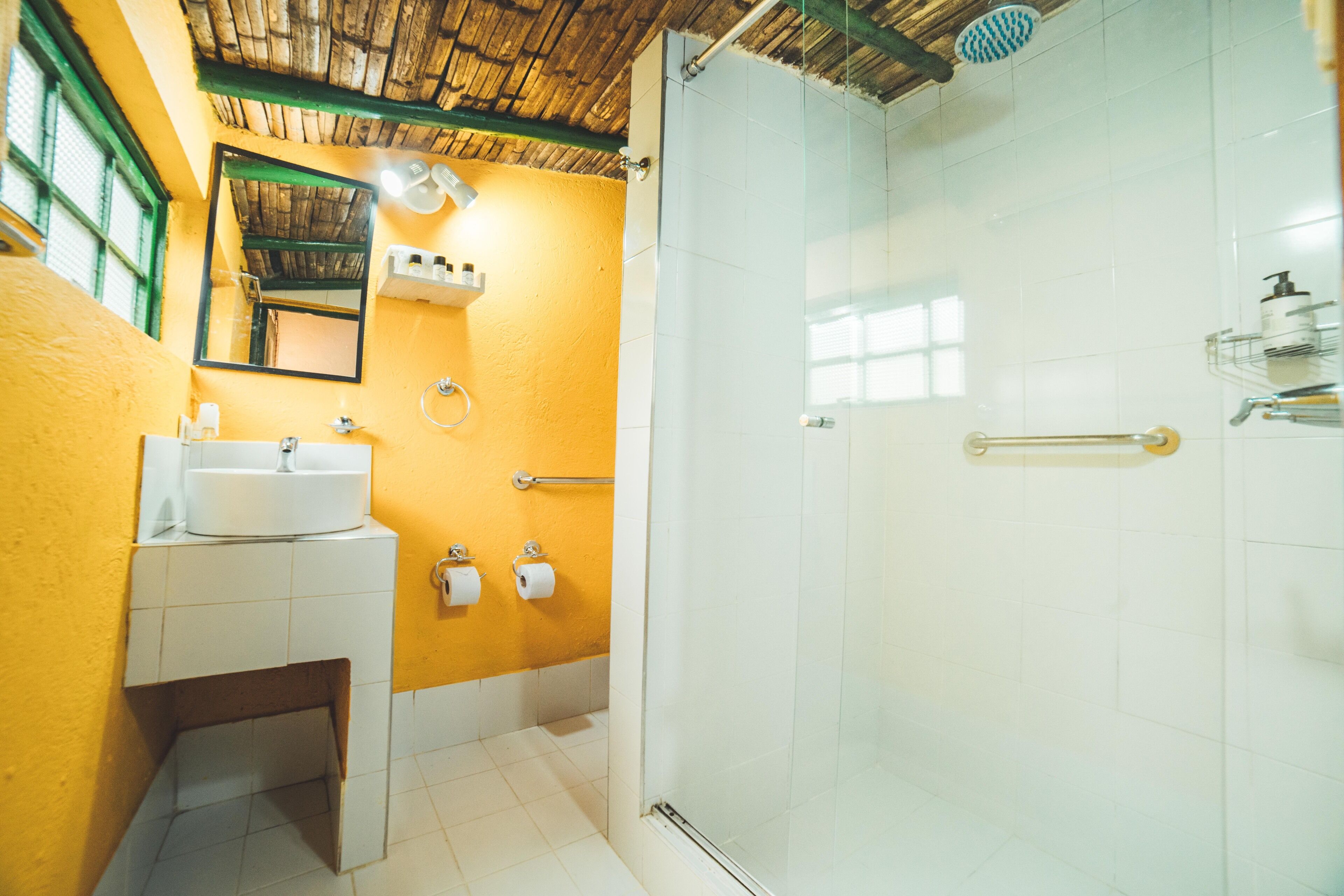 A bathroom with a yellow wall, a white sink, a mirror, and a glass-enclosed shower.