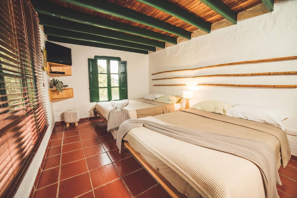 Een slaapkamer met twee bedden, een houten plafond, een betegelde vloer en een raam met luiken.