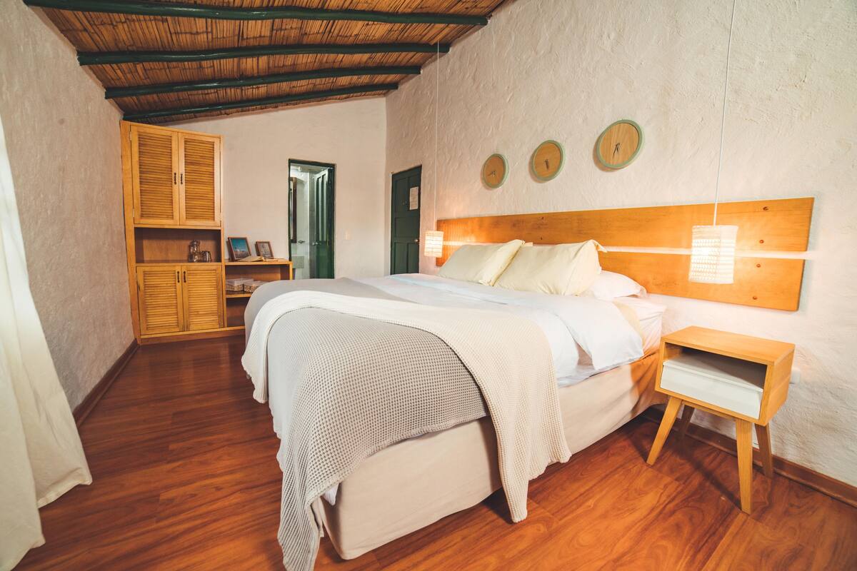 Een slaapkamer met een houten bed, een nachtkastje, een kledingkast en een deur die naar een andere kamer leidt.