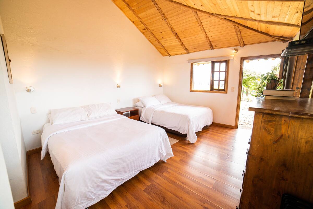 Een kamer met twee bedden, houten vloer, houten plafond en een raam met uitzicht op groen.