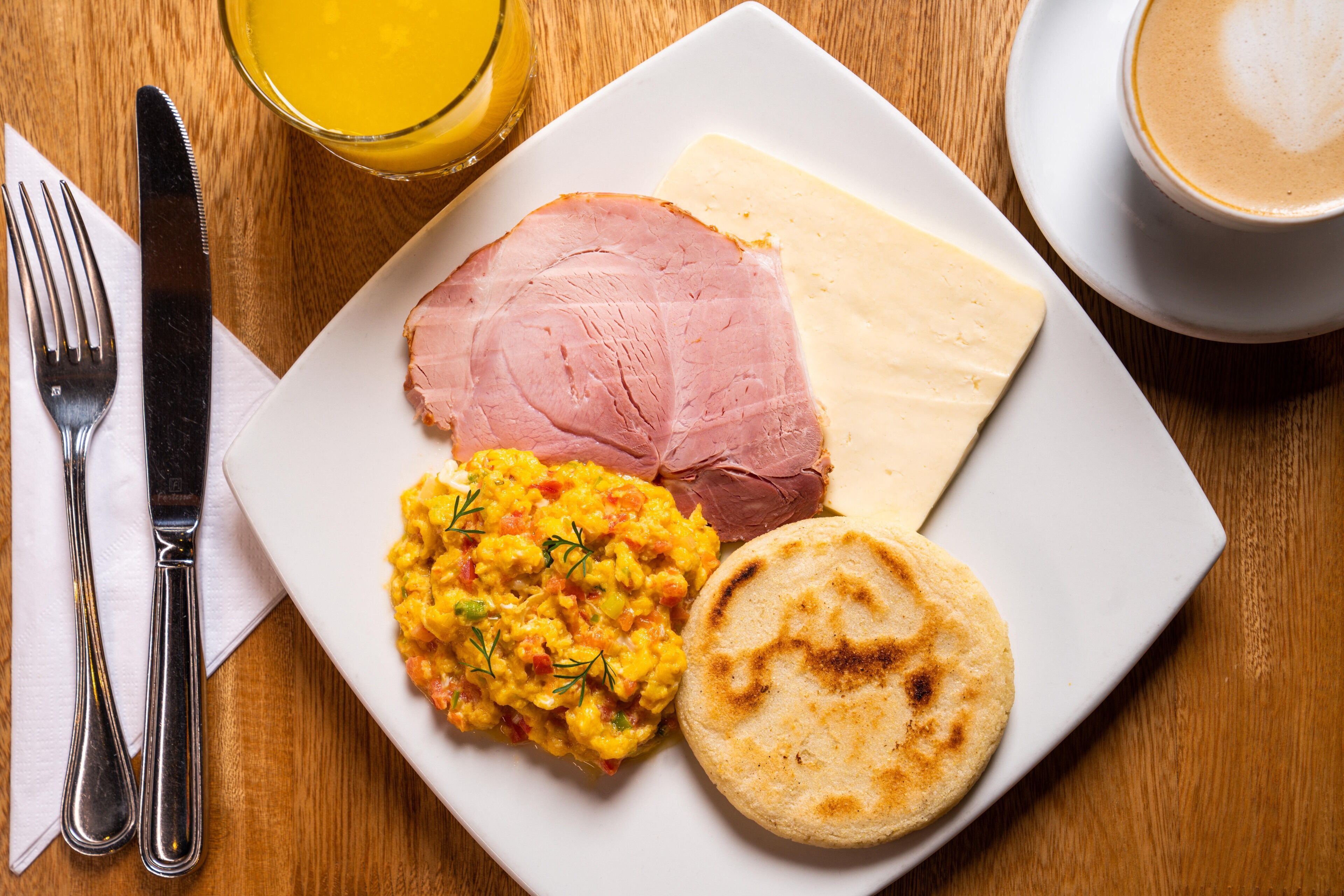 Un plato con jamón, huevos revueltos y un pan plano sobre una mesa de madera.