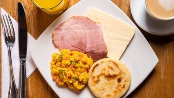 Un plato con jamón, huevos revueltos y un pan plano sobre una mesa de madera.