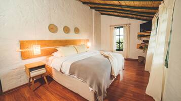 A bedroom with a wooden bed, a nightstand, a window with curtains, and a wall clock.