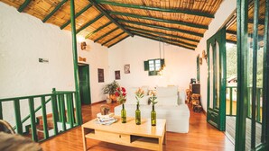 Ruime kamer met een houten vloer, een witte bank en een houten salontafel met drie groene flessen.