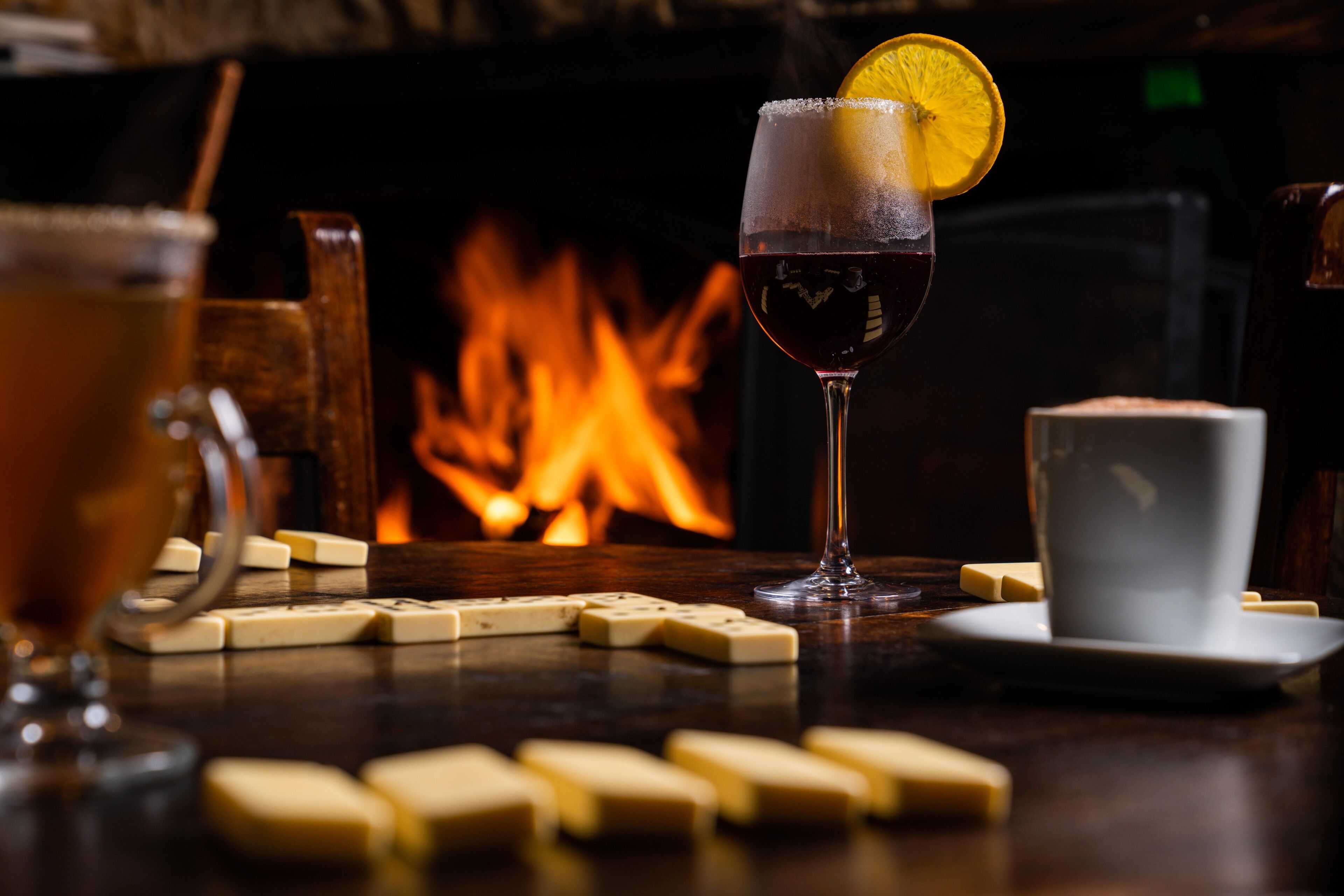A bar setting with a glass of red wine, a white cup, and dominoes on a table.