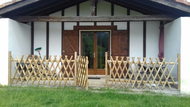 A wooden gate with a lattice design in front of a building with a wooden door and a glass window.