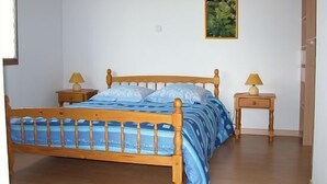A bedroom with a wooden bed, two bedside tables, a nightstand, and a framed picture on the wall.