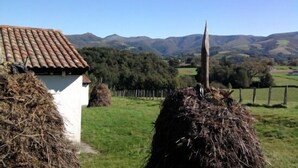 A rural landscape with a white building, hay bales, and a distant mountain range.