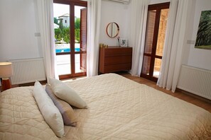 A bedroom with a large bed, a dresser, a mirror, and a view of a swimming pool through a glass door.