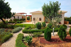 A residential area with two houses, a well-maintained garden, and a pergola structure.