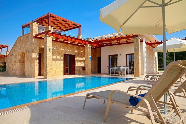 A poolside area with a stone building, a pool, and lounge chairs.