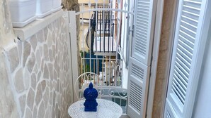 Un pequeño patio al aire libre con pared de piedra, mesa y sillas de metal blanco, una planta en maceta y un radiador blanco.