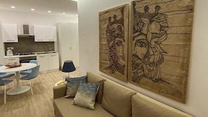 Una sala moderna con un sofá color beige, una mesa de comedor con sillas y una cocina al fondo.