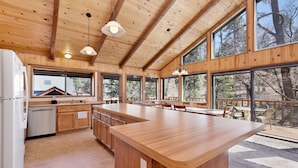 A spacious kitchen with wooden cabinets, a large island, and a view of the outdoors through large windows. - Wodehouse #1057 (Big Bear Lake)