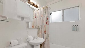Une salle de bain comprenant des toilettes, un lavabo et une baignoire, un rideau de douche et une fenêtre.