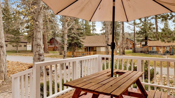 Une terrasse en bois avec une table de pique-nique et un parasol, entourée de rampes blanches et d’arbres.