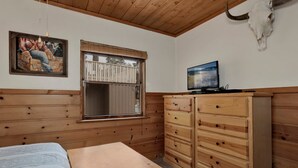 Une pièce comprenant un lit, une commode en bois, un tableau, une fenêtre et un téléviseur.