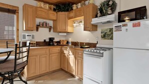 Une cuisine avec des meubles de rangement en bois, une cuisinière, un réfrigérateur et un coin repas avec une chaise.