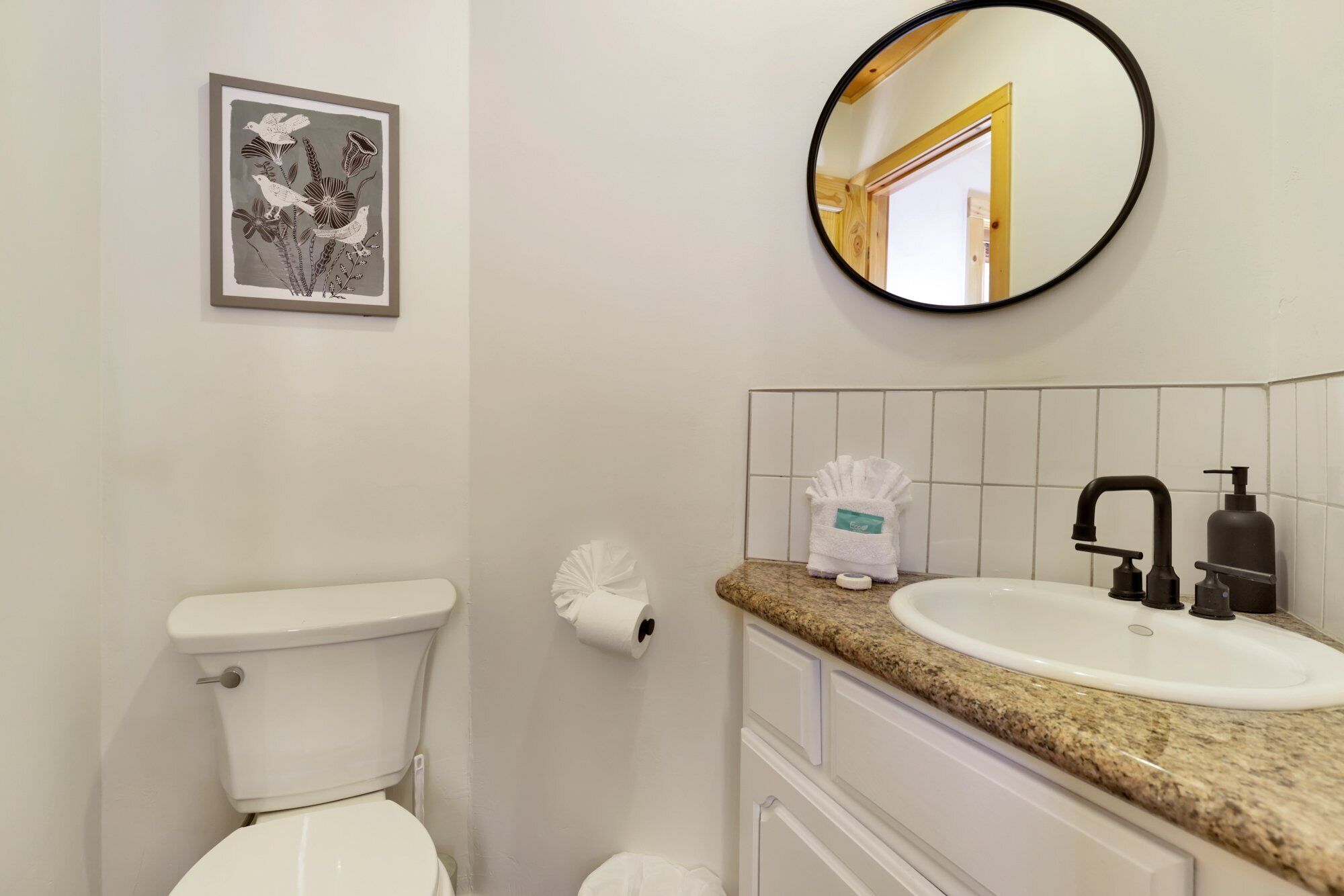 Une salle de bain équipée de toilettes, d’un lavabo et d’une œuvre d’art encadrée au-dessus des toilettes.