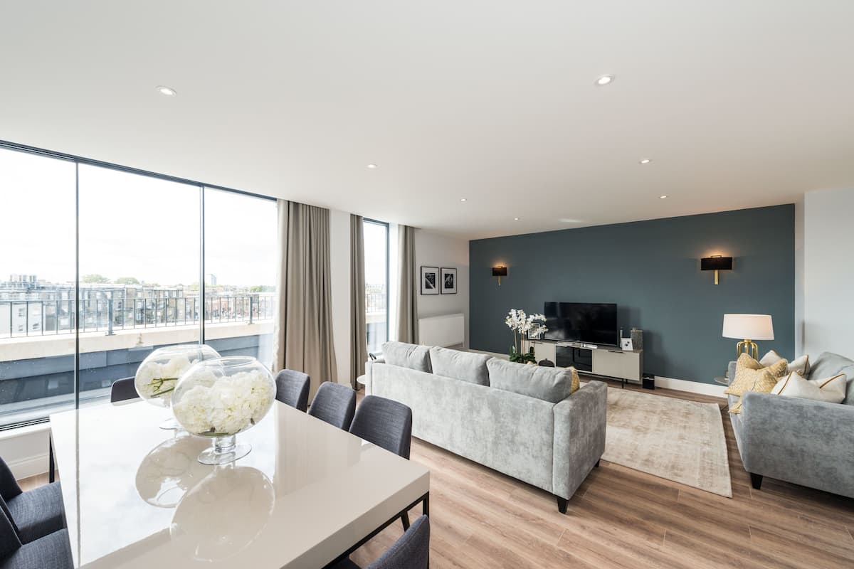 Een moderne woonkamer met een grijze bank, een eettafel met stoelen en een televisie op een dressoir.