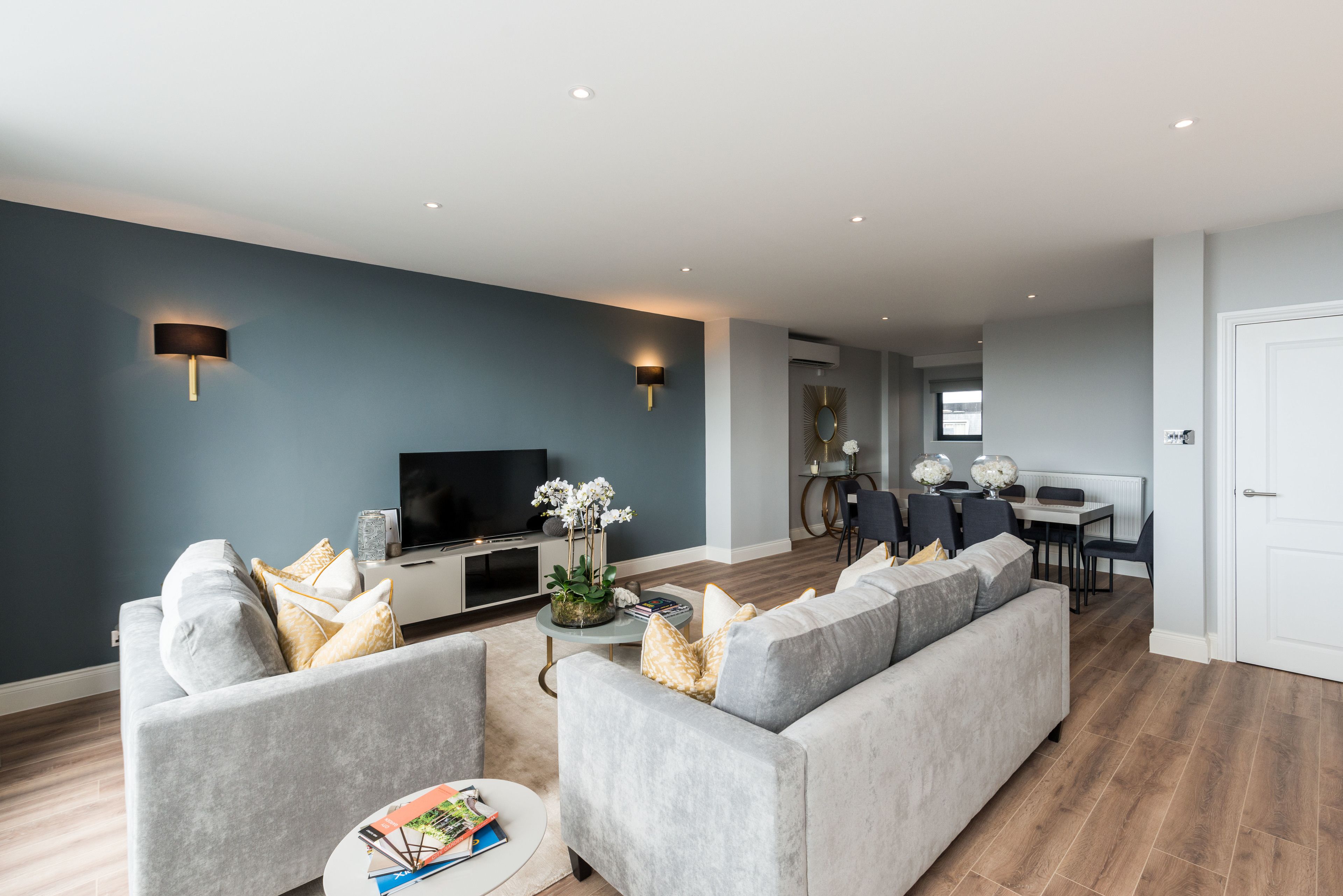 Una sala de estar moderna con un sofá gris, un televisor de pantalla plana y un comedor con mesa y sillas.