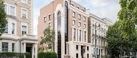 A multi-story building with a prominent central glass facade, a classical architectural style, and a street view with pedestrians.