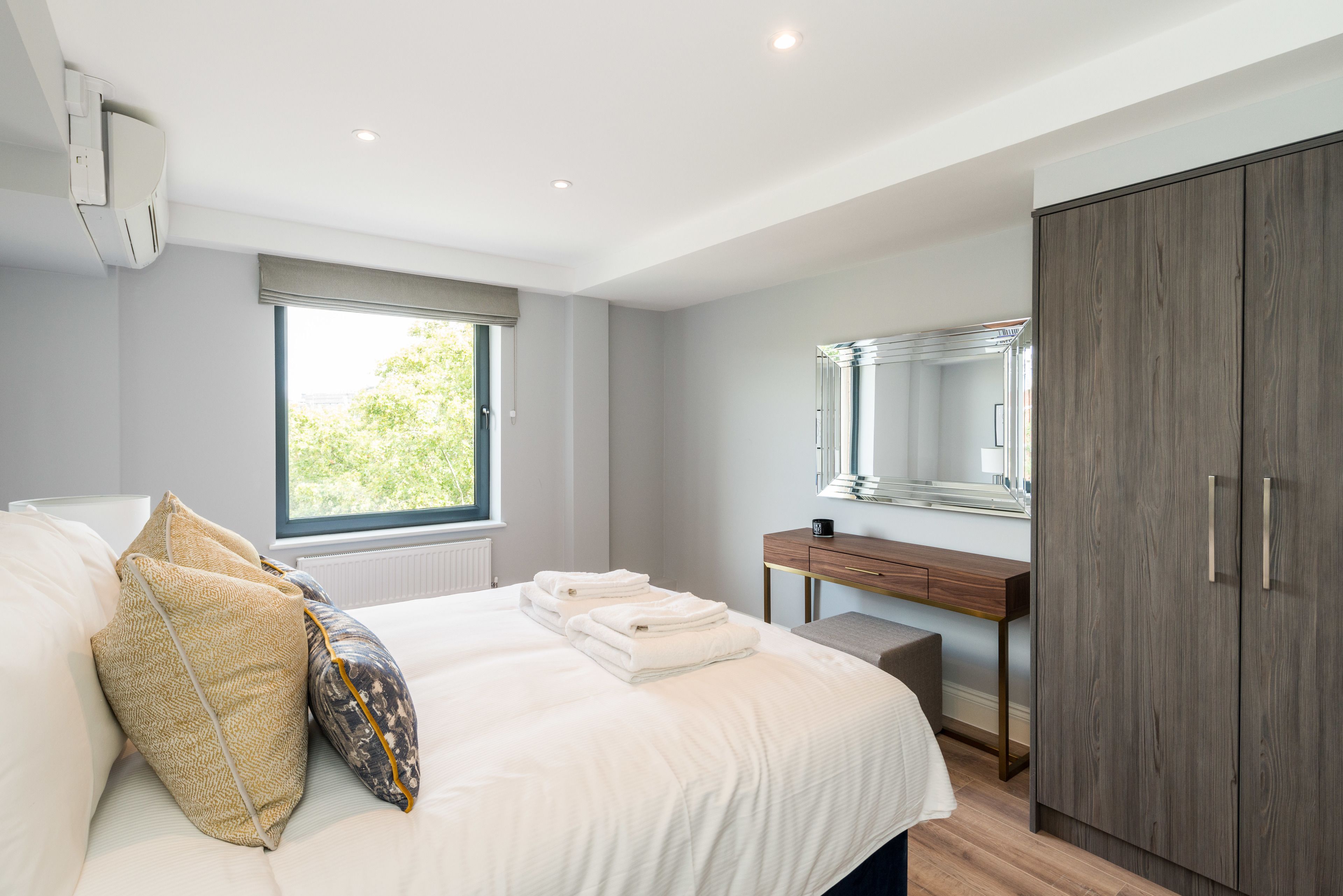 A modern bedroom with a large bed, a wooden desk, and a wardrobe.