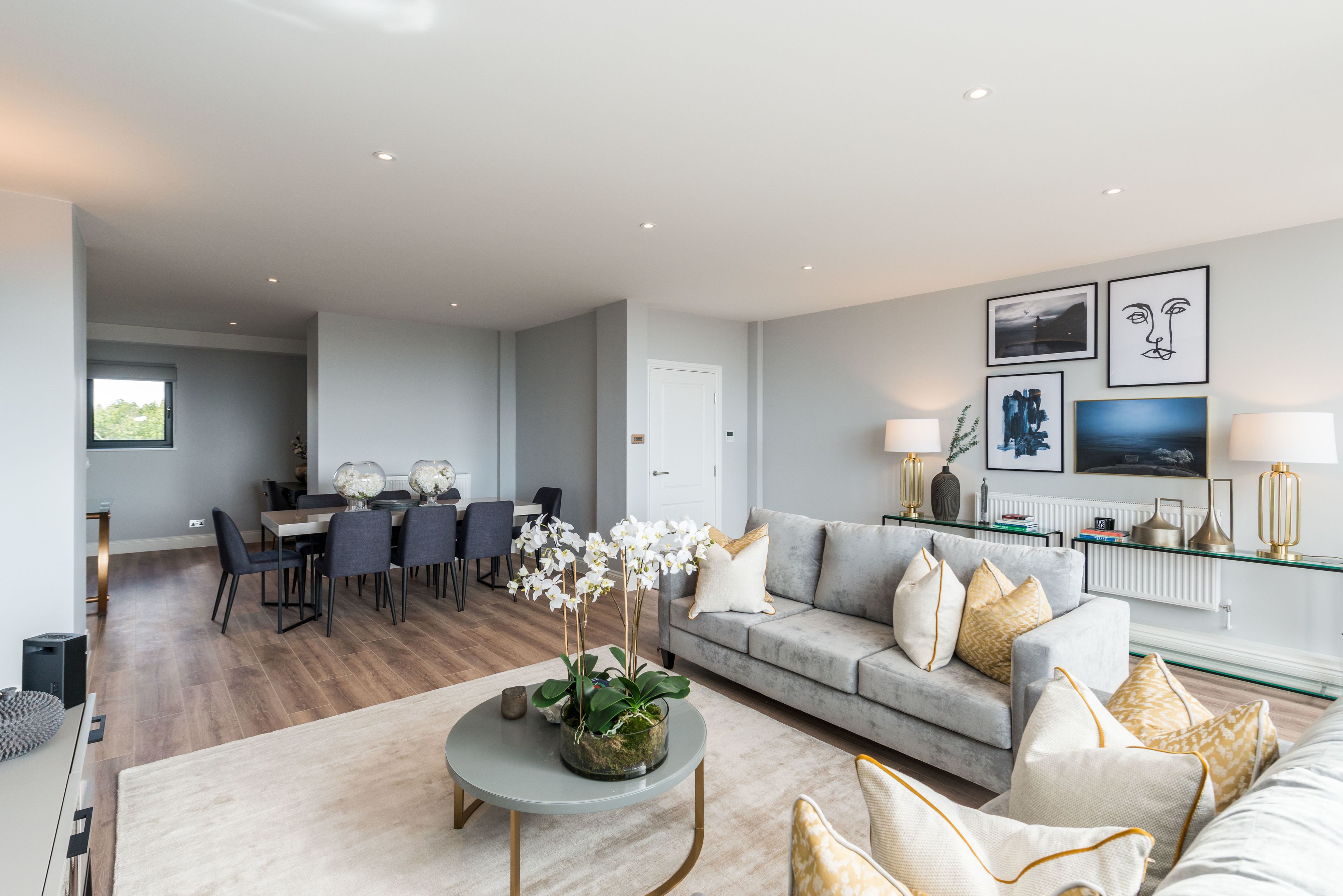 A modern living room with a grey sofa, a coffee table with a plant, and a dining area with chairs and a table.