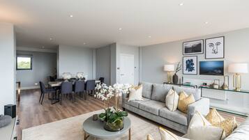 A modern living room with a grey sofa, a coffee table with a plant, and a dining area with chairs and a table.